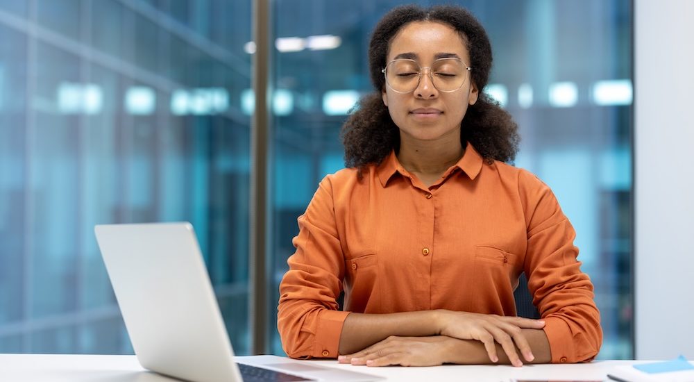 Young woman resting and relaxing inside office at workplace, businesswoman with closed eyes sitting and breathing with laptop, meditating.