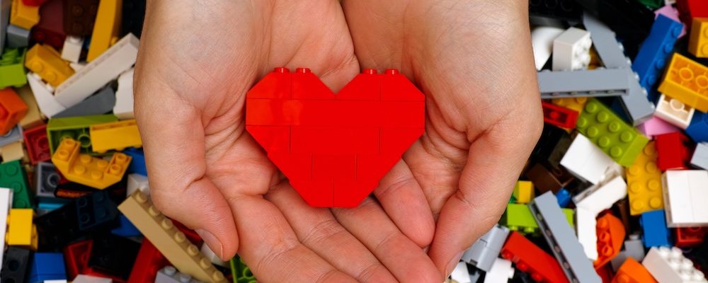 Tambov, Russian Federation - September 07, 2015 Lego red heart in woman hands with Lego blocks background. Studio shot.