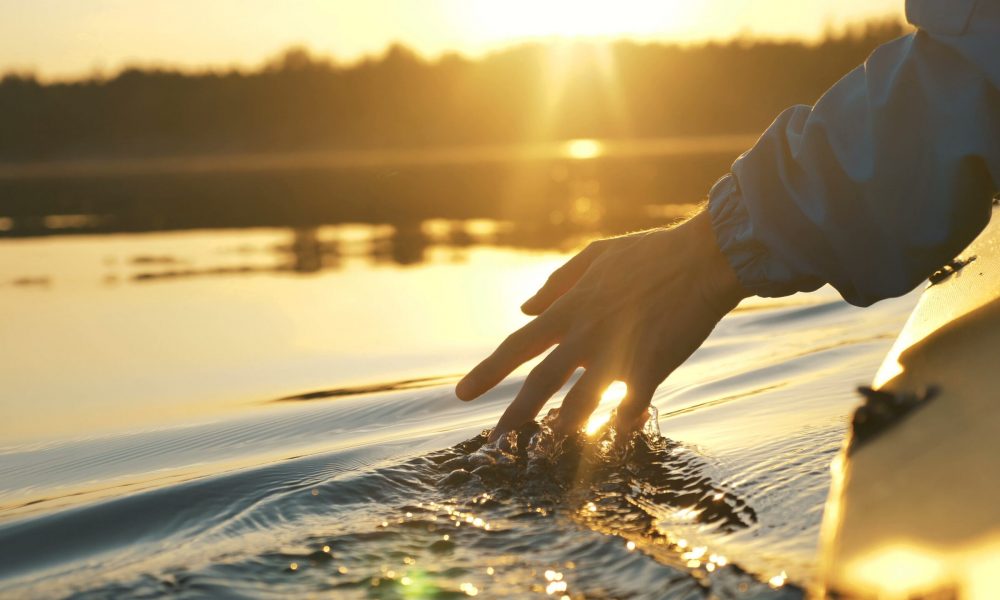 man puts fingers down in lake kayaking against backdrop of golden sunset, unity harmony nature
