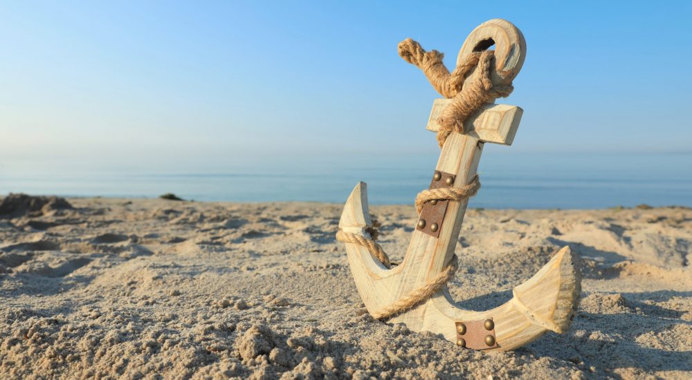 Wooden anchor with rope on sand near sea. Space for text