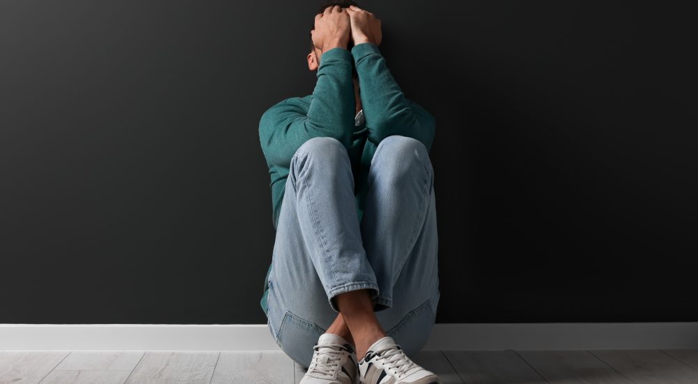 Upset man sitting on floor near black wall