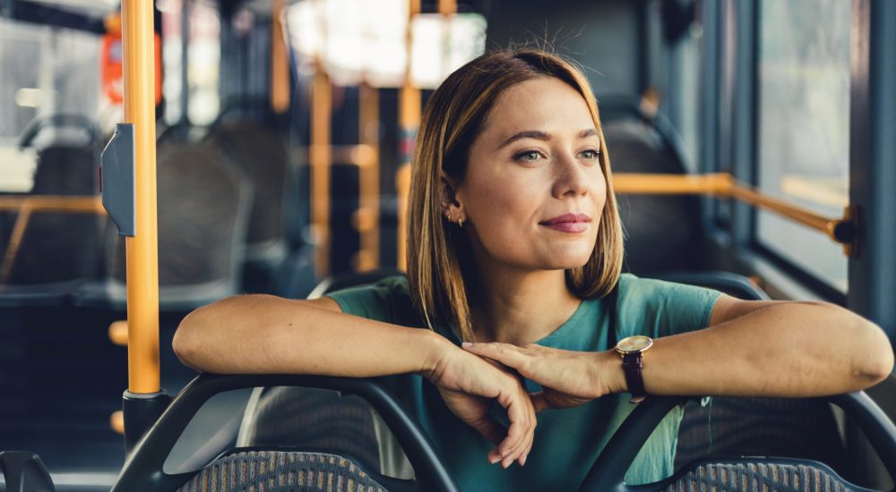 Beautiful woman sitting on the public bus. Woman traveler contemplating outdoor view from window of bus. Young lady on commute travel to work sitting in bus or train.